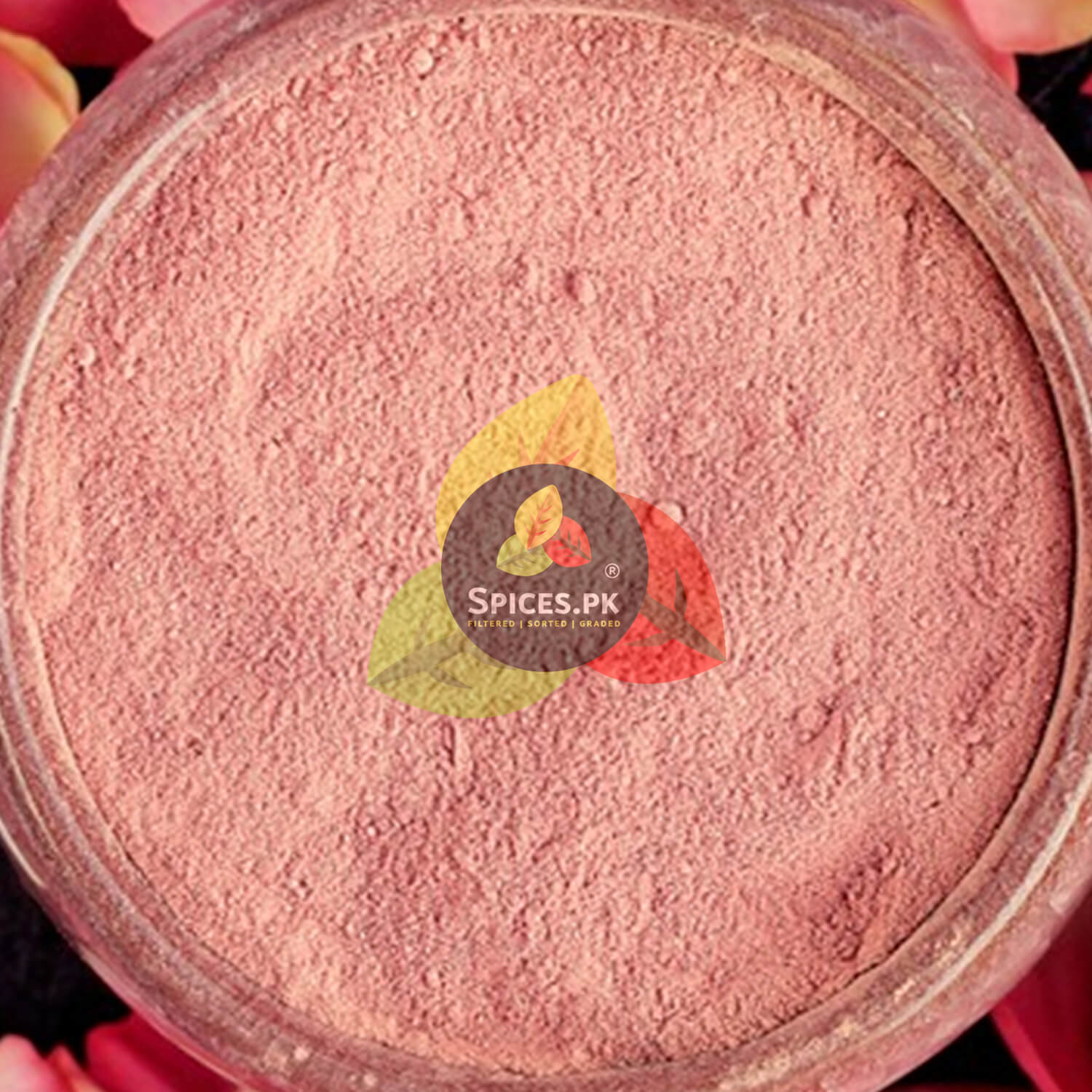 A white ceramic bowl filled with finely ground pink rose petal powder and a spoon, surrounded by dried petals.