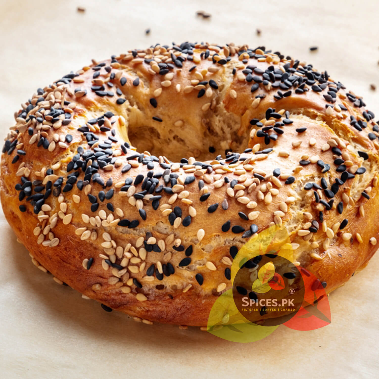 Freshly baked bagel topped with premium black and white sesame seeds, demonstrating the culinary uses of Spices.pk organic kalay til.Bagel with sesame and black sesame seeds on a light background, branded with 'Spices.PK'.