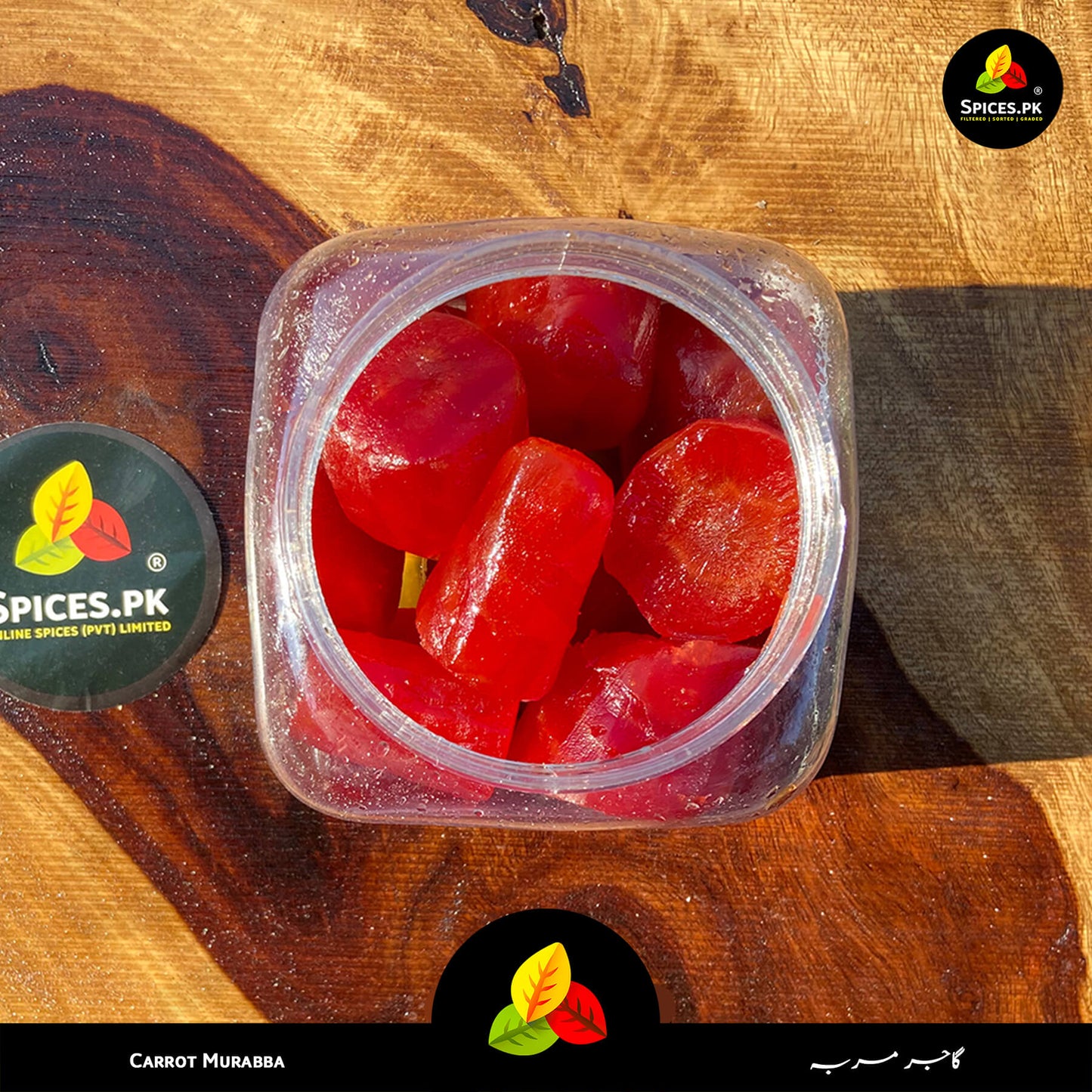 Top-down view of premium Carrot Murabba (Gajar ka Murabba) thick slices in a transparent jar by Spices.pk, showcasing its bright red color and sweet syrup texture.Jar of red carrot murabba on a wooden surface with 'Spices.PK' branding.
