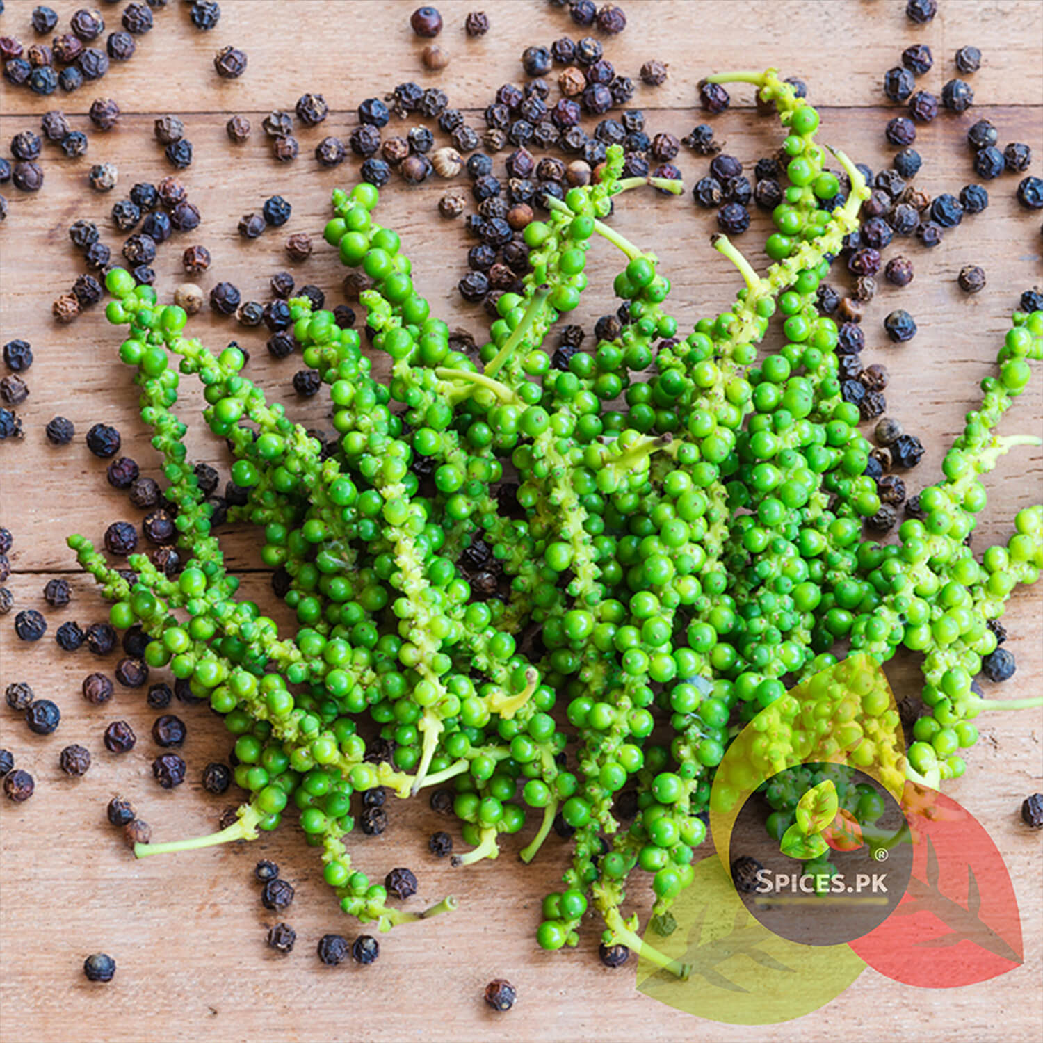 Fresh green peppercorns on the vine alongside dried black peppercorns on a wooden surface, showing the natural harvest process.