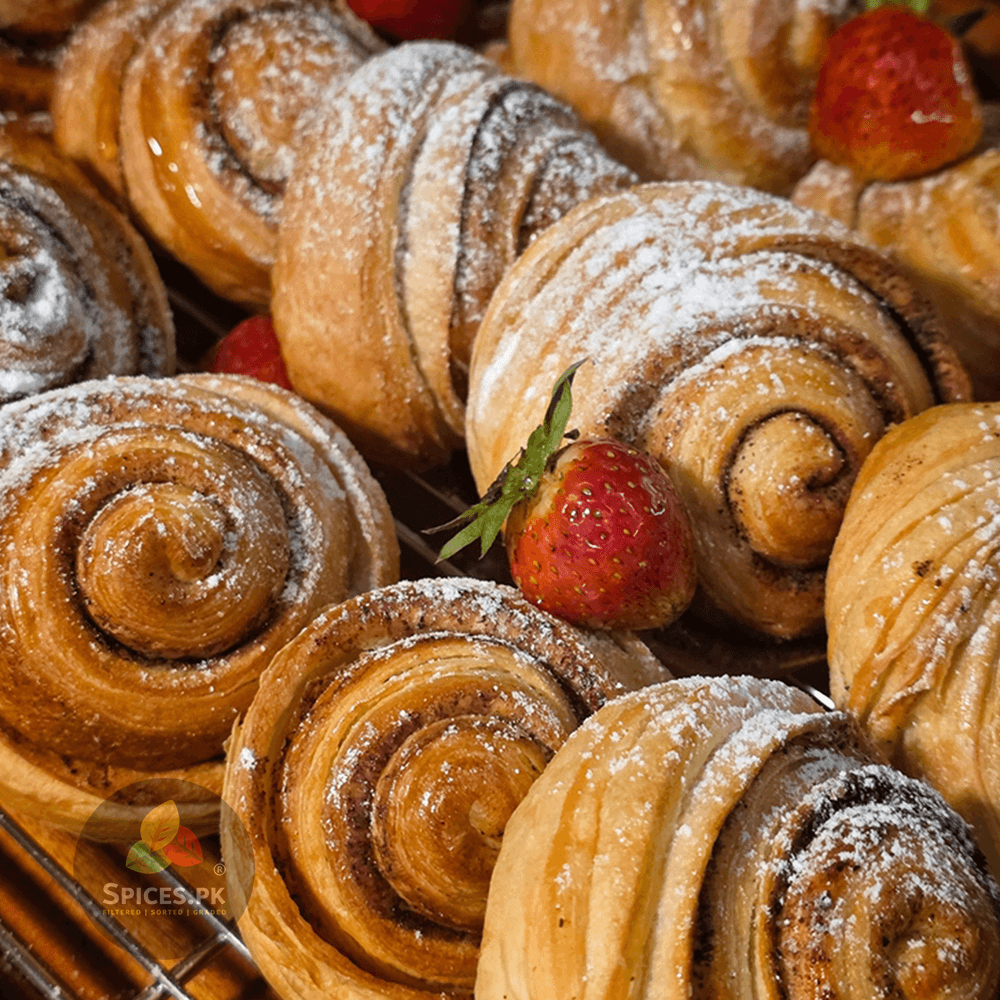 Freshly baked cinnamon rolls dusted with powdered sugar and topped with strawberries, highlighting Spices.pk baking spices.