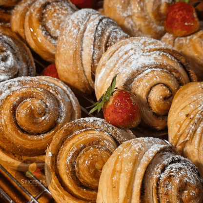 Freshly baked cinnamon rolls dusted with powdered sugar and topped with strawberries, highlighting Spices.pk baking spices.