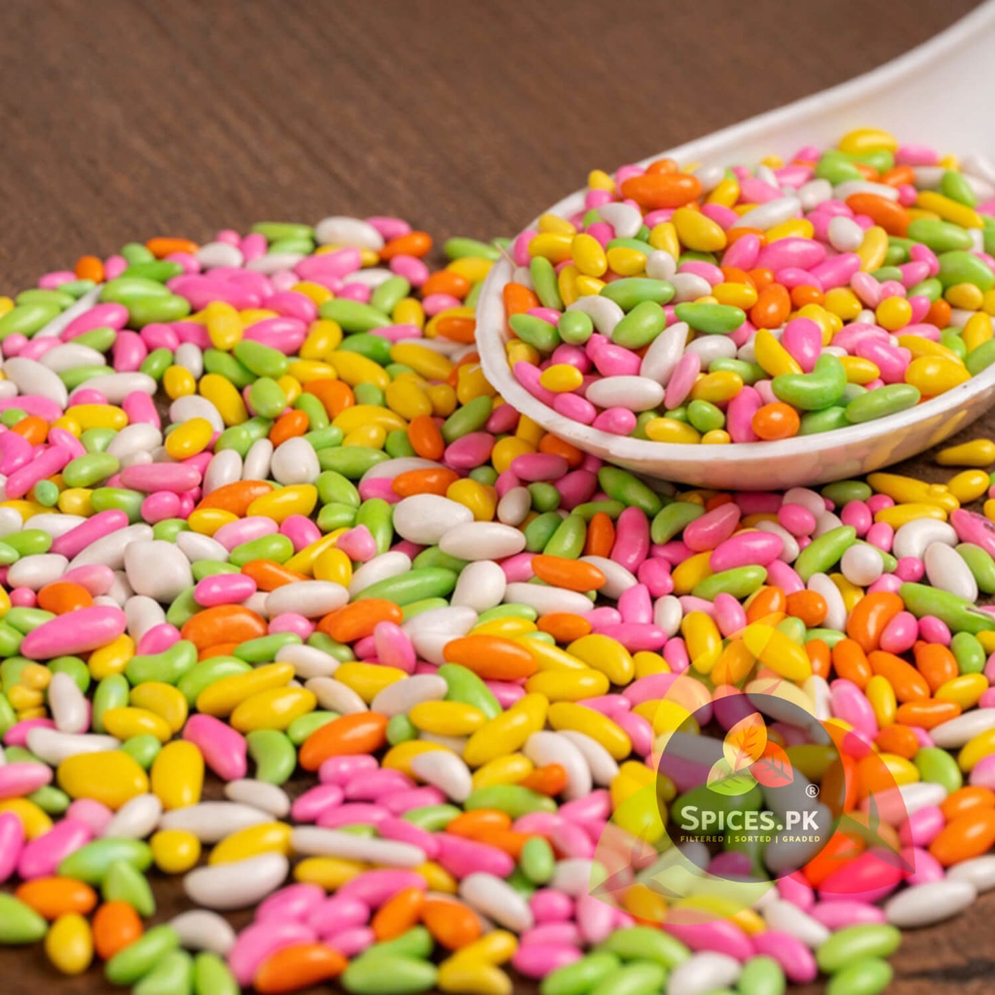 Close up of a white spoon with colorful sweet fennel seeds (Meethi Saunf) on a wooden table. Delicious after-meal mouth freshener.