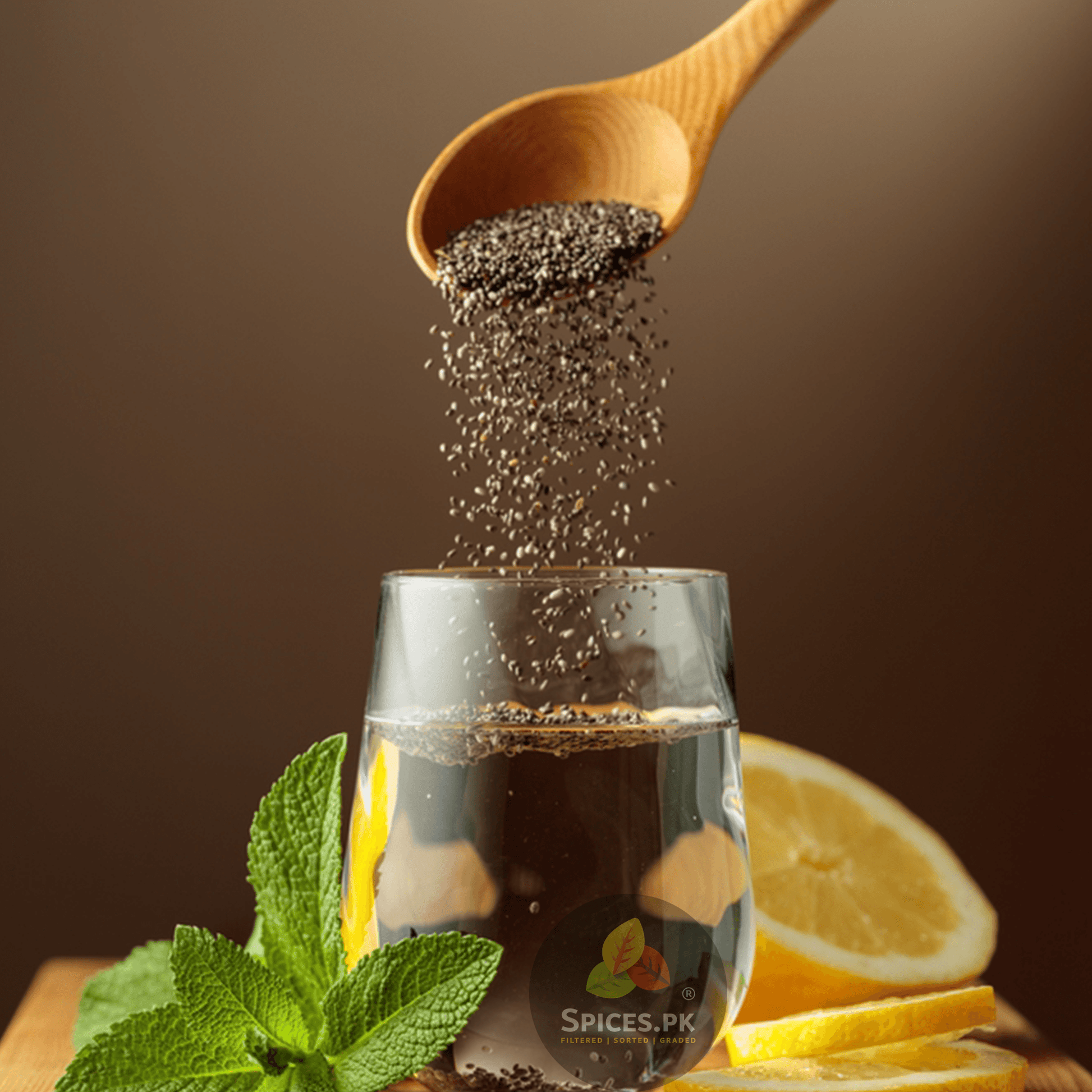 Organic chia seeds being poured from a wooden spoon into a glass of water with lemon and mint for weight loss by Spices.pk.Wooden spoon pouring chia seeds into a glass with lemon slices and mint leaves on a wooden board.