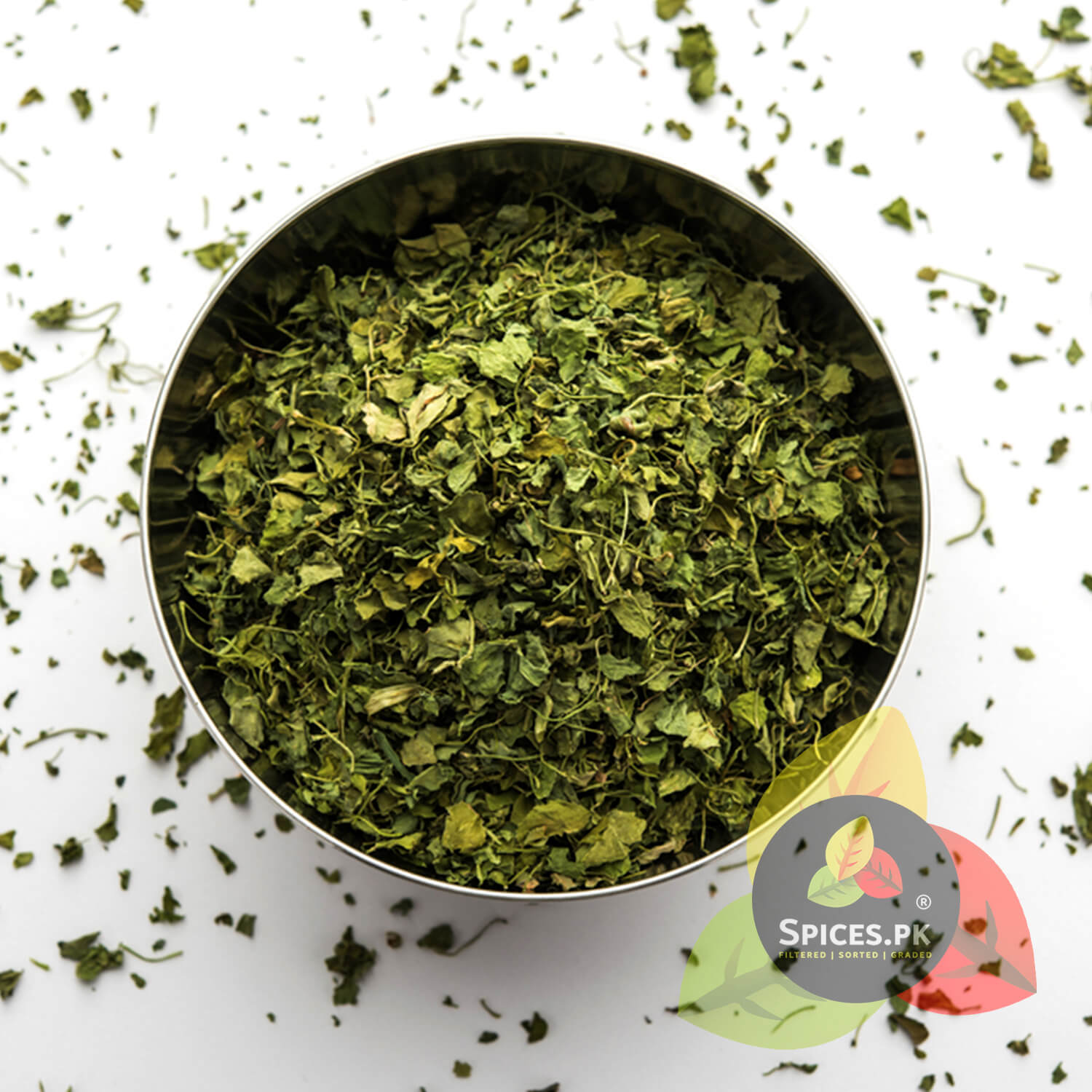 Dry green leaves in a metal container with 'Spices.PK' branding on a white background.Top-down view of filtered and graded premium Kasuri Methi dried leaves in a stainless steel bowl by Spices.pk