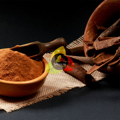 High-quality aromatic cinnamon powder in a rustic clay bowl with a wooden scoop and whole cinnamon bark.