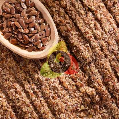Macro view of whole alsi seeds in a wooden spoon placed over finely ground organic flaxseed powder texture.Wooden scoop filled with flaxseeds on a bed of ground flaxseed with Spices PK logo.