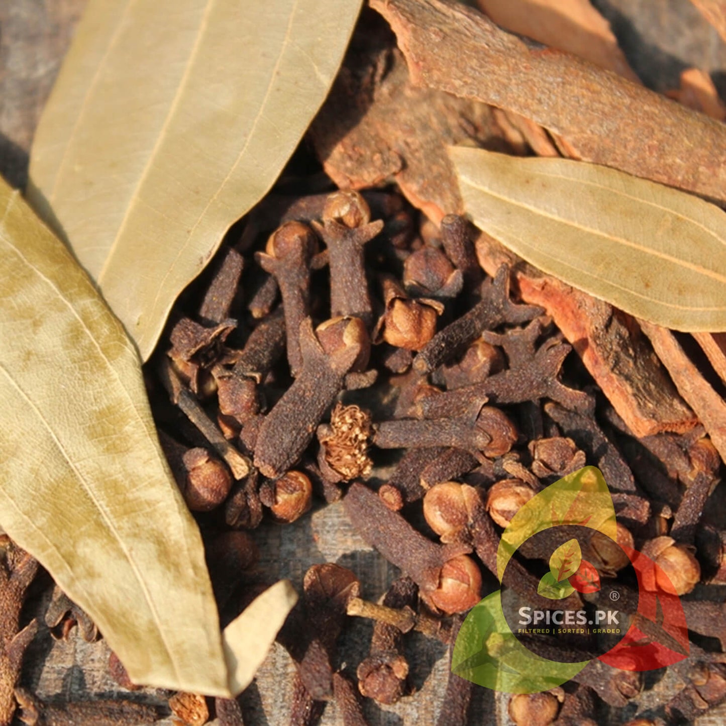 Detailed close-up view focusing on whole cloves, authentic cinnamon sticks, and dried bay leaves (Tej Patta) from the Spices.pk garam masala collection. Raw, natural whole spice ingredients for ultimate flavour.